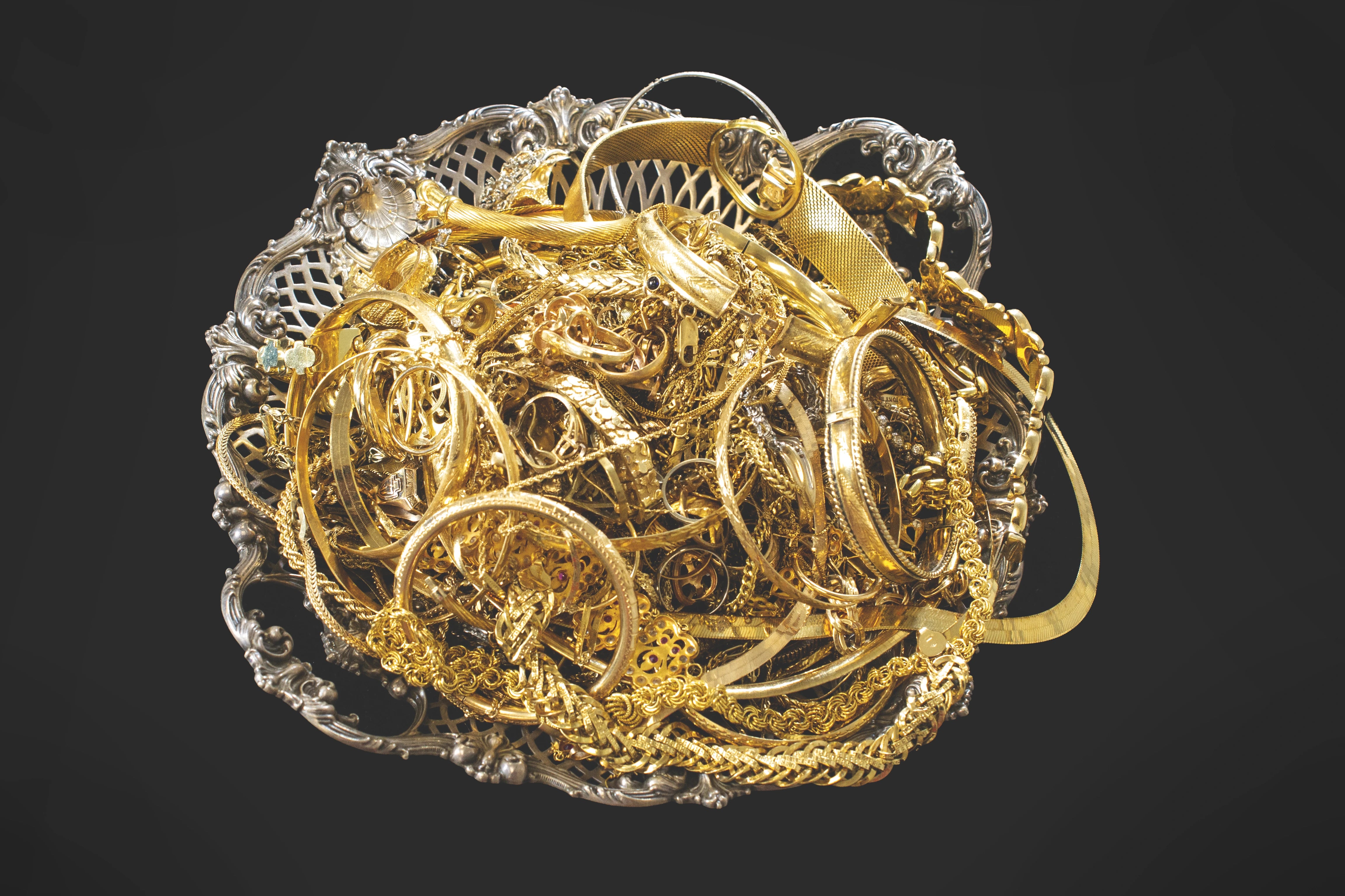 A pile of assorted gold jewelry, including rings, necklaces, and bracelets, resting on an ornate silver filigree dish - sell your gold jewelry to DJP Jewelers & Luxury Buyers in Houston